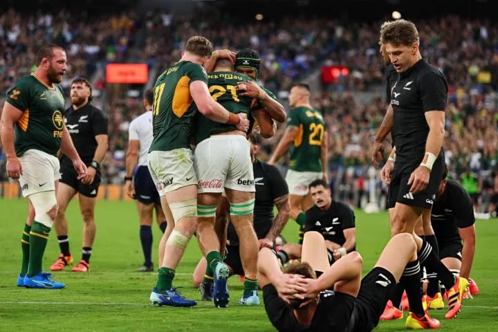 Springboks players celebrate a try in Baltimore while All Blacks lie on the turf and Beauden Barrett walks away